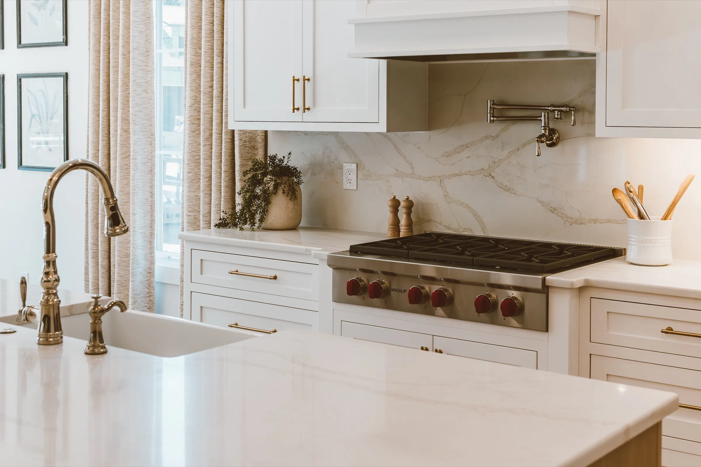 White kitchen with a marble island, brass fixtures and a Wolf range