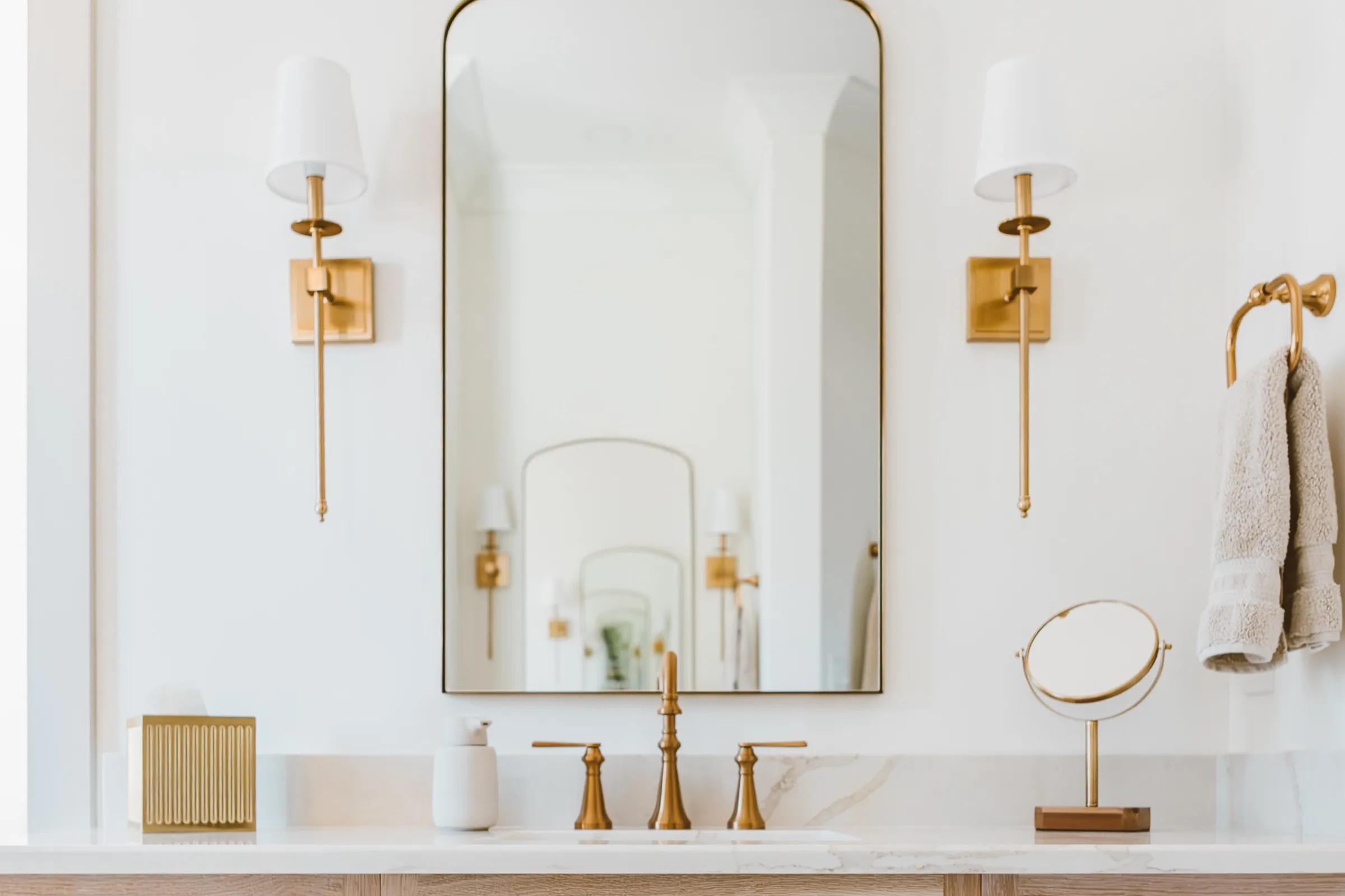 White oak vanity with brass sconces and an arched mirror